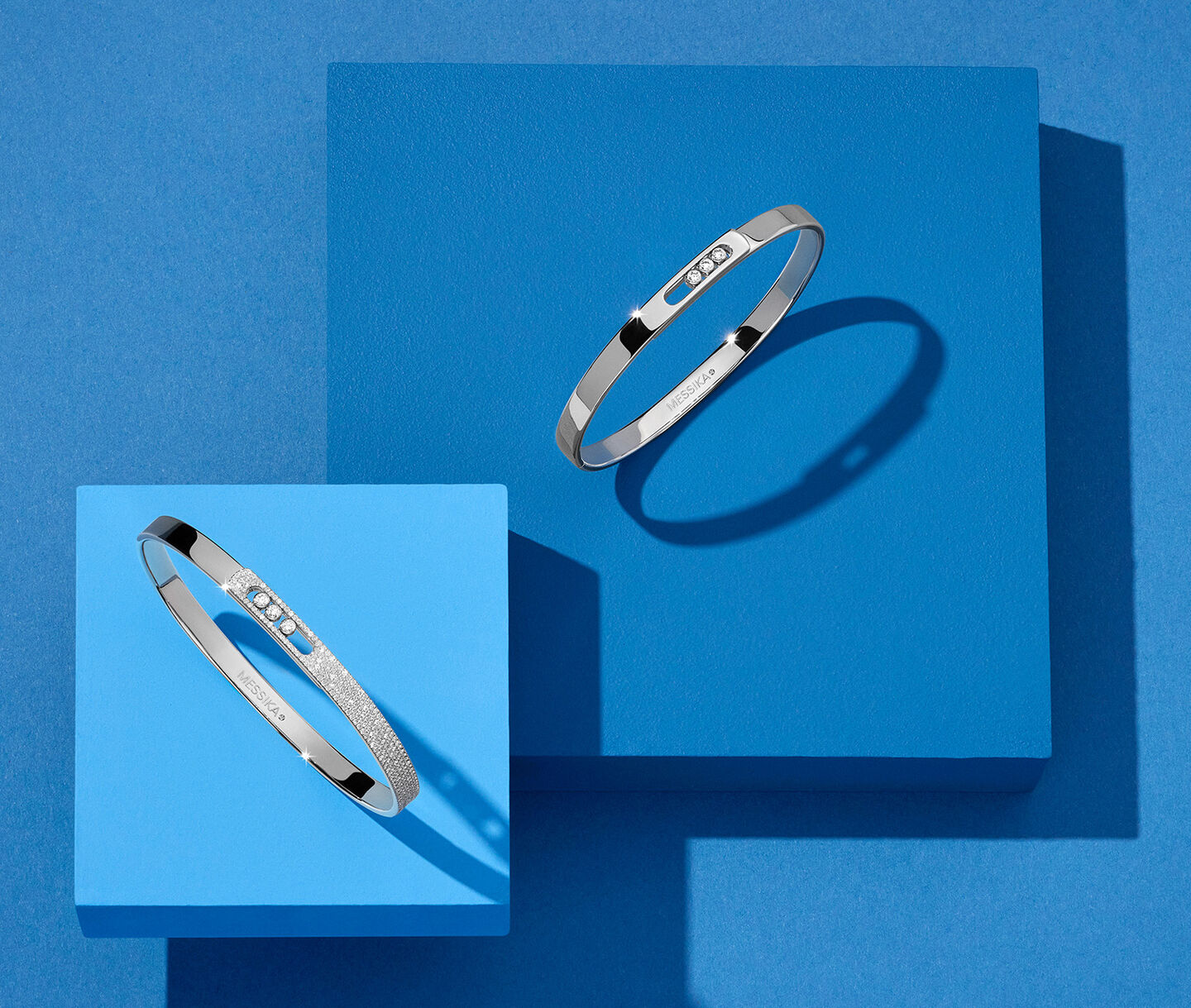 White gold and diamond Messika bangles on a blue background.